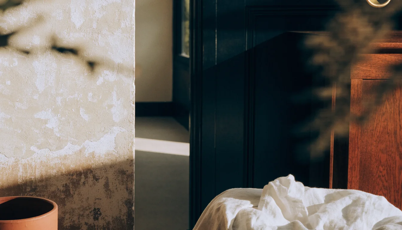 A quiet sunlit threshold: weathered plaster, a glazed doorway, linen and warm wood